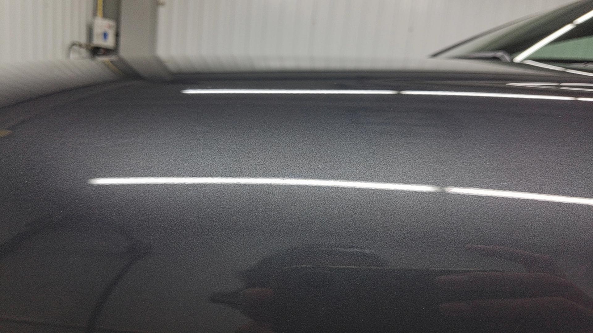 Macro of a dark car paint panel in a detailing bay crossed by one hard horizontal LED light bar